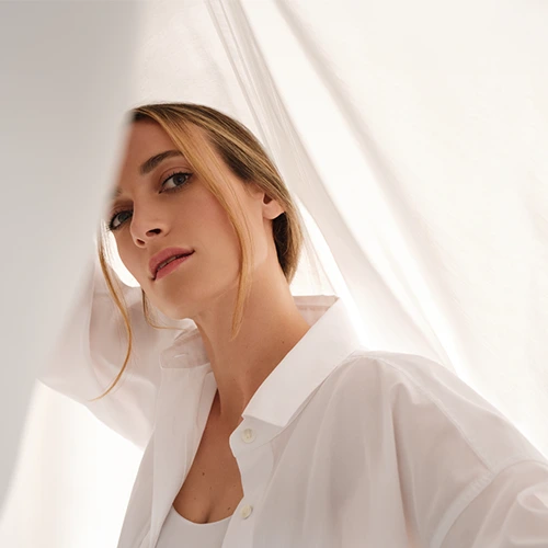 A woman posing between white sheets.