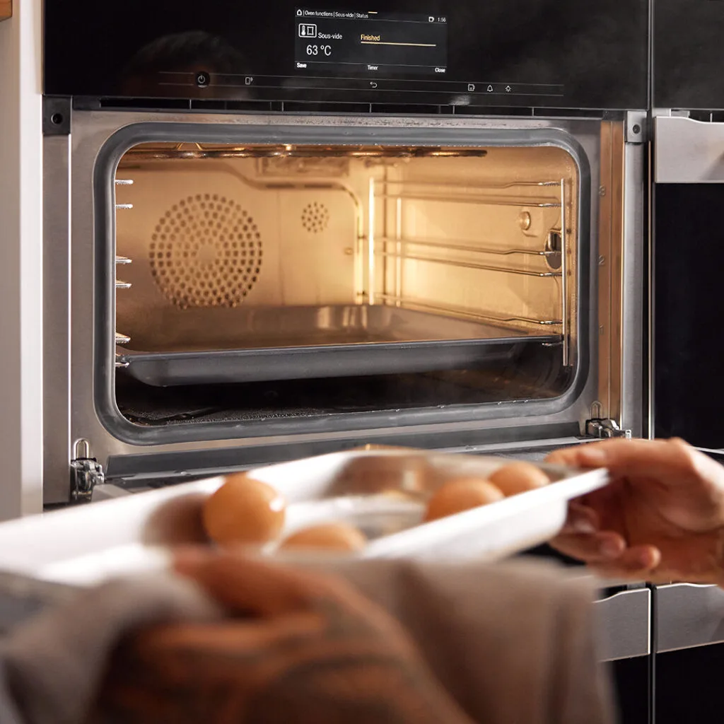 Chef Michael Meredith putting a tray of eggs in a Miele oven to be cooked.
